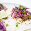 A vibrant image showing Cast-Iron Seared Flank Steak Tacos filled with juicy, caramelized flank steak, a colorful tangy red cabbage slaw and a creamy cheese sauce, all nestled in warm flour tortillas.