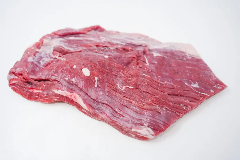 A raw flank steak displayed on a clean white background, highlighting its long, flat shape and distinct muscle fibers, ideal for absorbing marinades and quick cooking.






