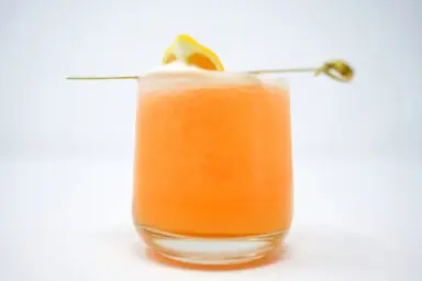 A refreshing Cantaloupe Cooler cocktail in a glass, featuring a vibrant blend of vodka, honey, and smooth cantaloupe purée, garnished with a slice of lemon on the rim, set against a clean backdrop.