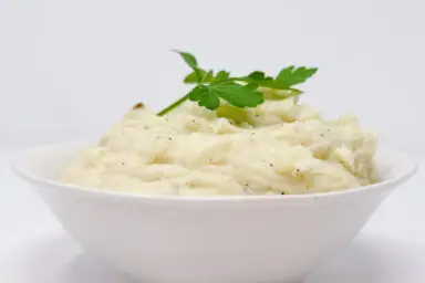 A bowl of rich elephant garlic mashed potatoes, topped with a melting pat of butter and sprinkled with fresh chives, highlighting its creamy texture and subtle garlic taste.
