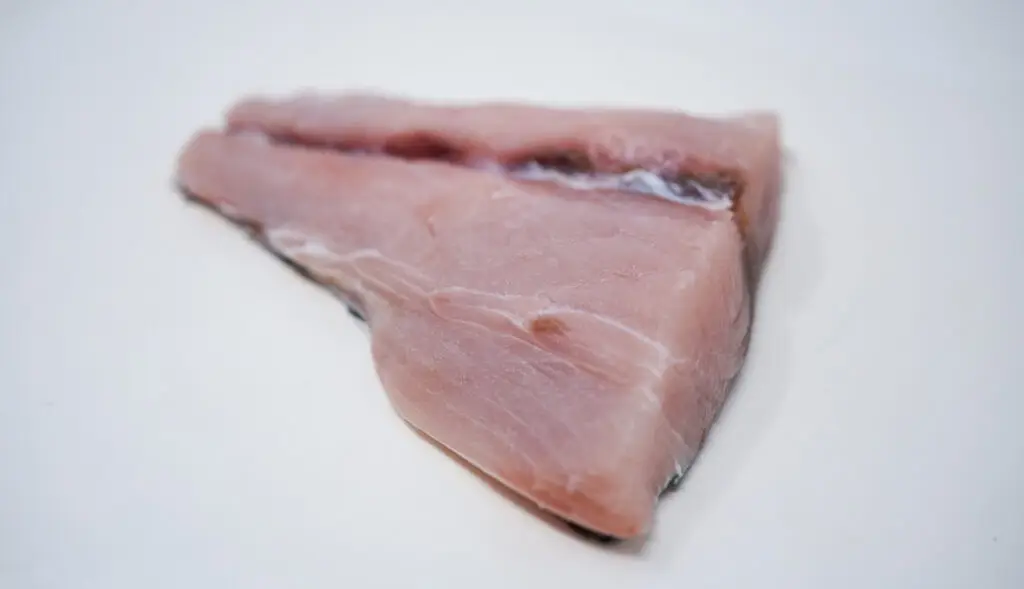 A fresh amberjack fillet displayed on a clean white background, showcasing its thick, firm texture and pale pink color, ideal for culinary presentations.