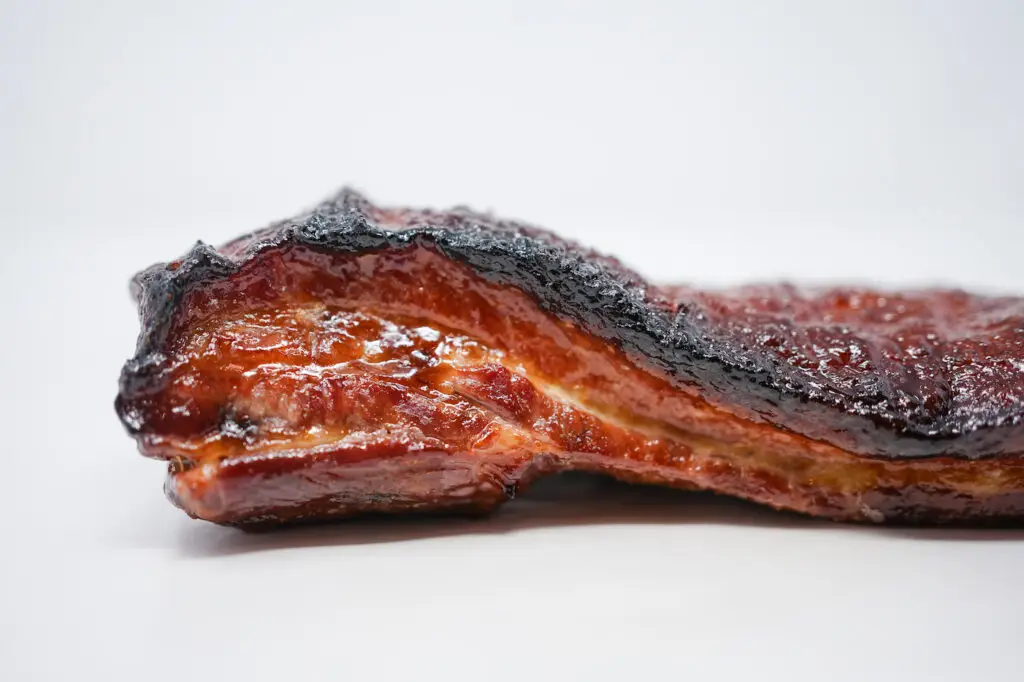 A whole slab of crispy pork belly on an all-white background, its golden-brown, crackling surface glistening, showcasing the succulent and juicy meat underneath, ready for serving.
