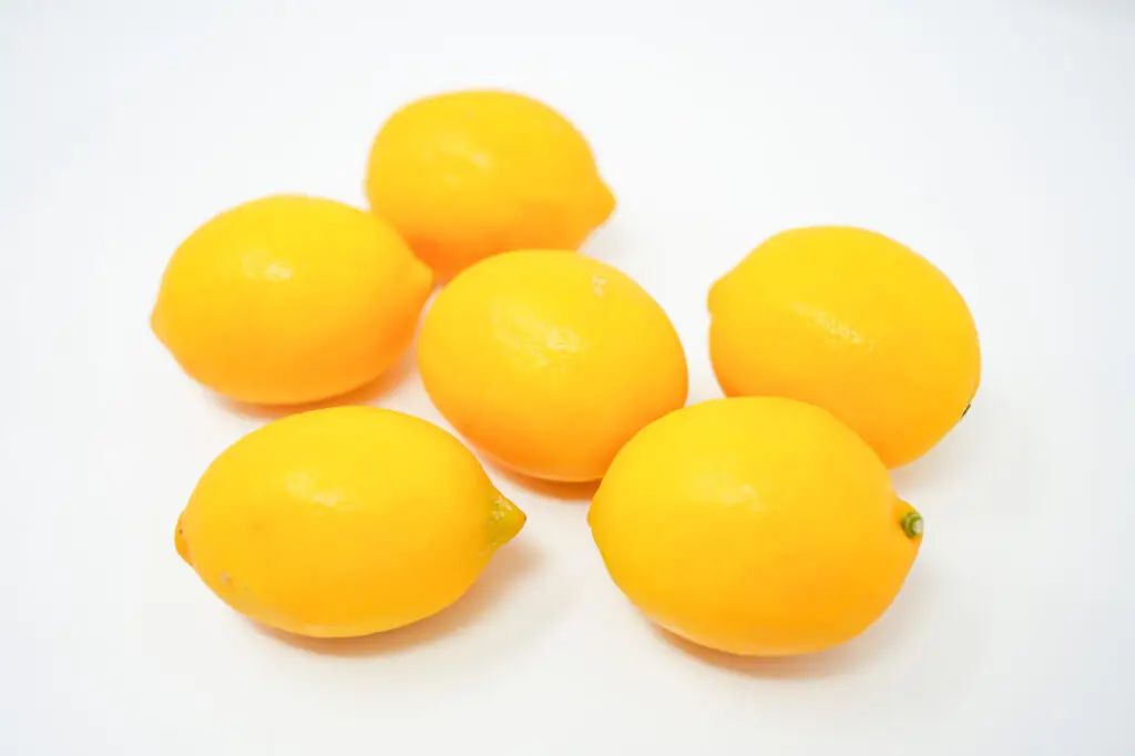 A cluster of ripe Meyer lemons, their deep yellow to slightly orange skins glowing, nestled together with vibrant green leaves, showcasing their unique round shape and smooth, thin peel characteristic of this sweet and aromatic citrus fruit.