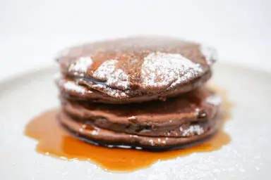 A stack of rich mocha pancakes drizzled with glossy coffee syrup, showcasing the perfect blend of chocolate and coffee flavors, served on a white plate.
