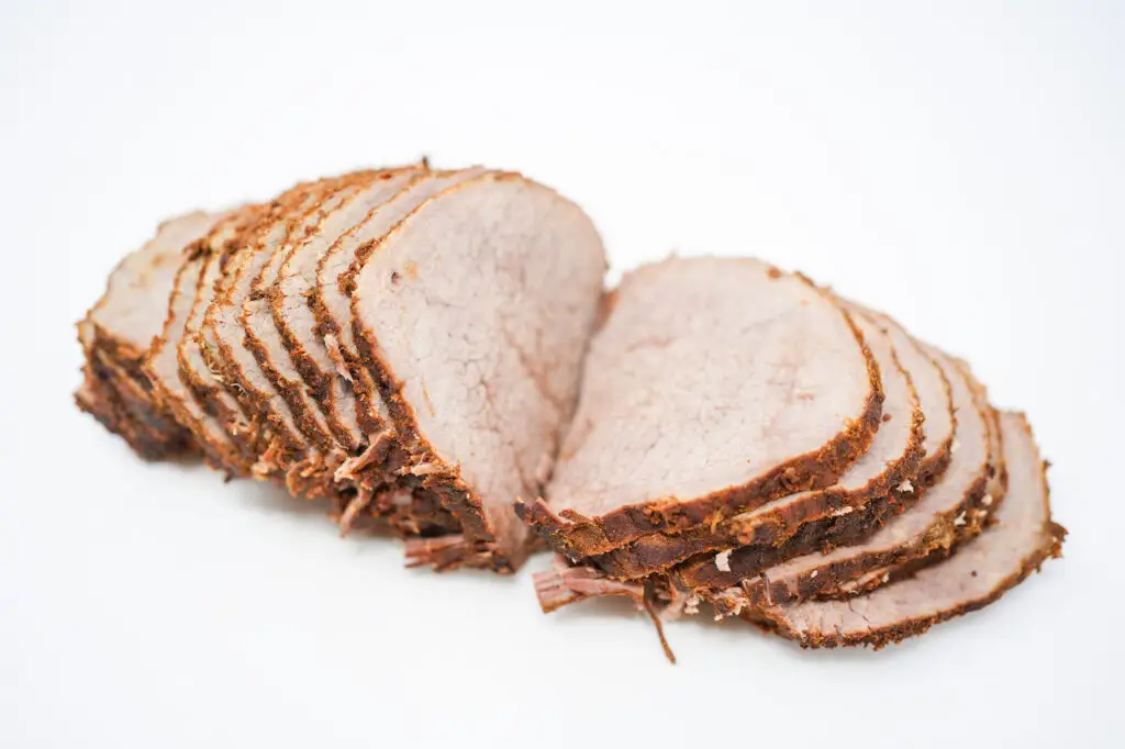 Slices of Moroccan-spiced roast beef arranged neatly on a white background, showcasing the rich, reddish-brown crust from the blend of spices, with the tender, juicy interior of the meat visible, embodying the aromatic and flavorful essence of Moroccan cuisine.