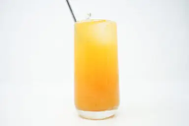 A tall glass of Peach Thyme Bellini, featuring layers of golden peach puree and effervescent Prosecco, garnished with a fresh thyme sprig for a sophisticated touch.