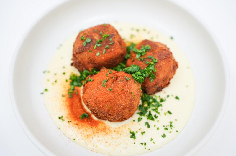 A plate of Chicken and Potato Croquettes with Gruyere Cheese Sauce, featuring crispy, golden croquettes resting on a bed of creamy cheese sauce, garnished with chopped parsley and paprika.