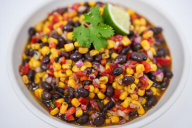 A colorful image of Chilled Corn and Black Bean Salad, featuring bright yellow corn, black beans, red bell pepper, and green cilantro, tossed in a shiny, zesty lime dressing.