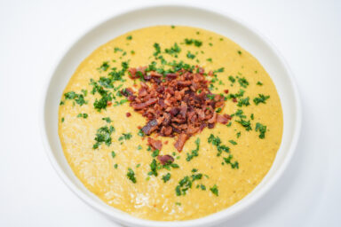 A bowl of Creamy Corn and Bacon Bisque garnished with crispy bacon bits and fresh parsley, showcasing its rich and velvety texture.