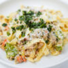 A plate of Creamy Italian Sausage and Shishito Pepper Tagliatelle, showcasing ribbons of pasta coated in a rich, creamy sauce dotted with slices of spicy Italian sausage and tender shishito peppers, garnished with fresh basil and a sprinkle of lemon zest.