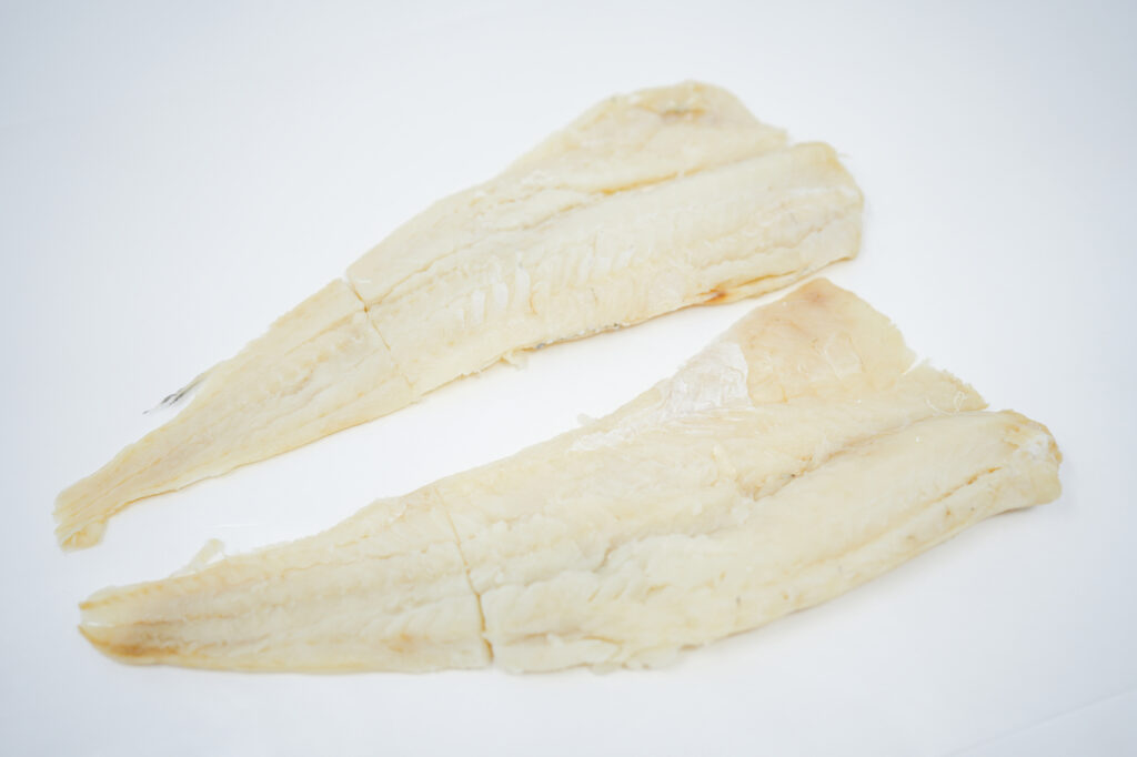 An image of salt cod, displaying dried, salted pieces of codfish with a pale, slightly translucent appearance, neatly arranged on a clean, white surface, emphasizing the textured, flaky exterior characteristic of the preservation process.






