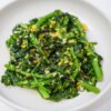 A vibrant dish of spicy garlic rapini, featuring bright green broccoli rabe sautéed with red pepper flakes and garnished with lemon zest, served in a white bowl.