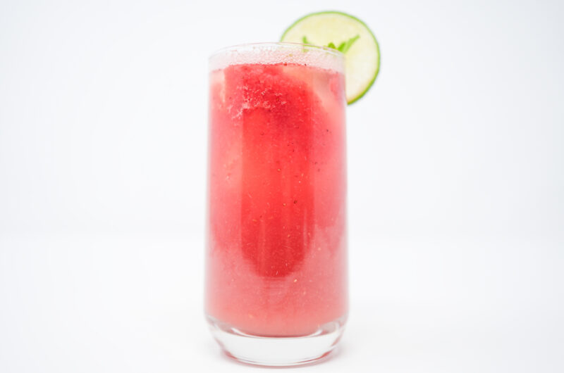 A vibrant pink Watermelon Mint Tequila Fizz in a clear glass, garnished with fresh mint leaves and a lime wedge, with fizzy bubbles rising to the top.