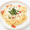 A plate of Brown Butter Garlic Angel Hair Pasta with cherry tomatoes, garnished with fresh basil leaves and grated Parmesan cheese.
