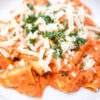 A plate of Garlic Butter Vodka Rigatoni, garnished with freshly grated Parmesan cheese and vibrant green basil leaves. The rigatoni pasta is coated in a rich, creamy sauce, with visible specks of garlic and a hint of red from the pureed tomatoes.
