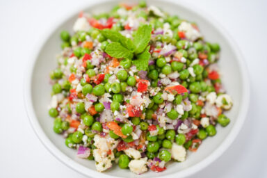 A vibrant bowl of Chilled Pea and Mint Salad with Feta, featuring sweet peas, diced red bell pepper, cherry tomatoes, red onion, fresh mint, and crumbled feta, all dressed with a tangy lemon dressing.