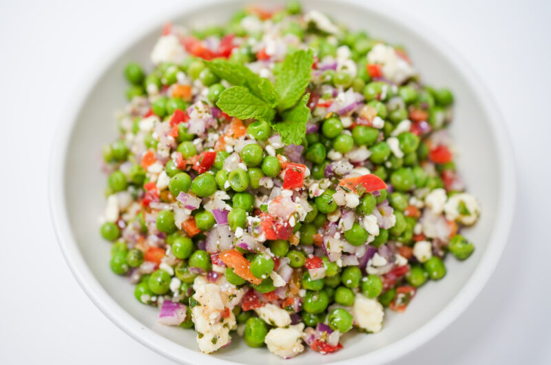 A vibrant bowl of Chilled Pea and Mint Salad with Feta, featuring sweet peas, diced red bell pepper, cherry tomatoes, red onion, fresh mint, and crumbled feta, all dressed with a tangy lemon dressing.
