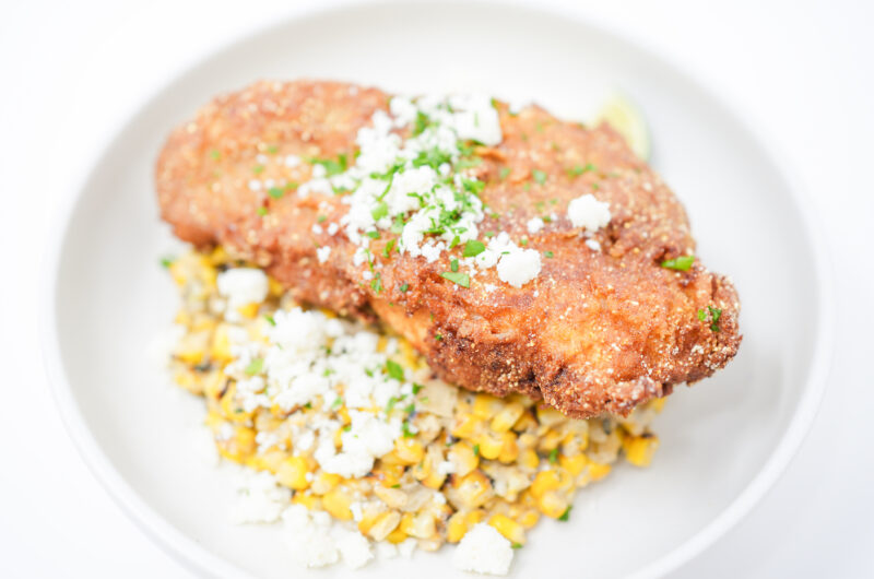 A plate of Southern Fried Catfish with Spicy Esquites, featuring golden, crispy catfish fillets alongside creamy, charred corn topped with crumbled cotija cheese, fresh cilantro, and lime wedges.