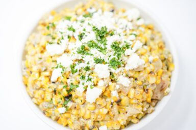 ChatGPT A vibrant bowl of Grilled Jalapeño and Vidalia Onion Esquites, featuring charred corn, jalapeños, and onions mixed with a creamy sauce, topped with crumbled cotija cheese and fresh cilantro.