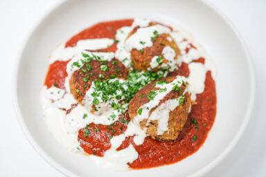 A bowl of Falafel Lamb Meatballs in rich tomato sauce, topped with a creamy tahini drizzle and garnished with fresh parsley