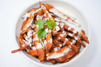 A plate of crispy, golden-brown paprika steak fries garnished with fresh parsley, served alongside a bowl of creamy, tangy passionfruit aioli. The vibrant colors and textures highlight the unique combination of smoky and tropical flavors.