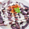 A plate of crispy ube fries drizzled with creamy mango aioli, garnished with chili powder.
