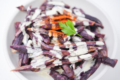 A plate of crispy ube fries drizzled with creamy mango aioli, garnished with chili powder.