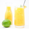 A refreshing glass of Mango Basil Agua Fresca, garnished with fresh basil leaves and a wedge of lime, featuring a bright yellow-orange color and served over ice cubes.